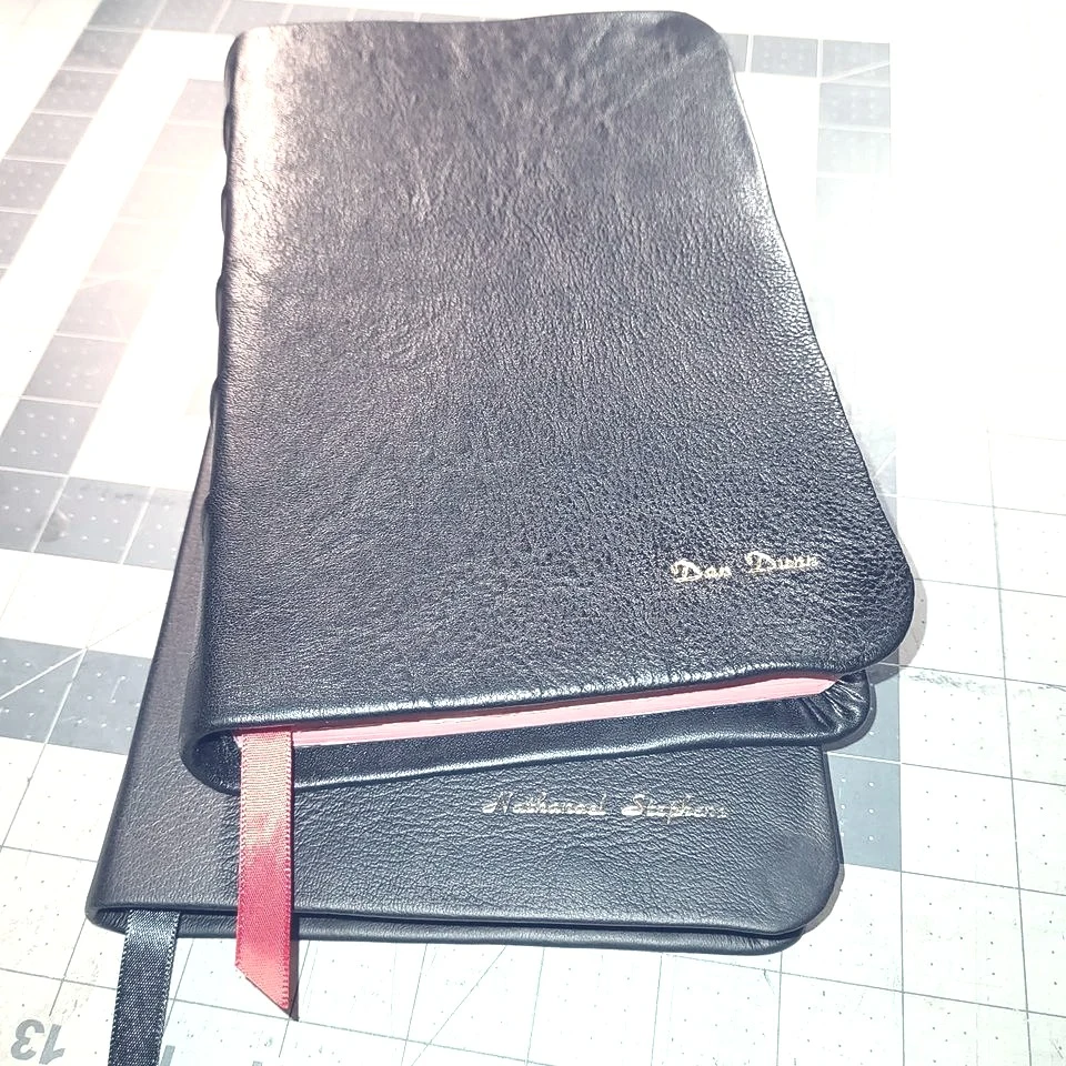 Two personalized black leather Bibles with contrasting page edges and ribbon markers.