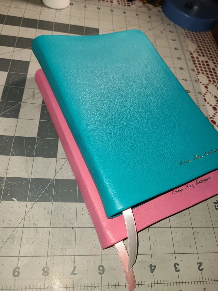 Turquoise and pink leather-bound books with personalized gold lettering and ribbon markers.